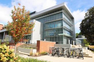 a glass building with a bike/scooter rack and a tree with fall foliage in front of it.