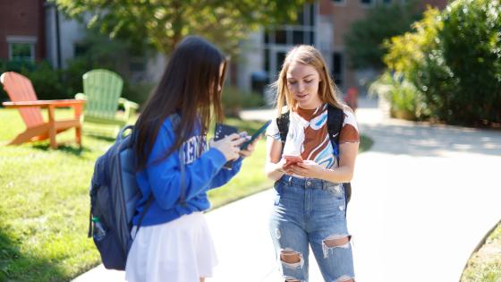 Two students outside looking at their smartphones